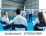 Aviation instructor explaining aircraft components to a group of diverse student pilots during a lesson inside a bright modern hangar at a flight training school