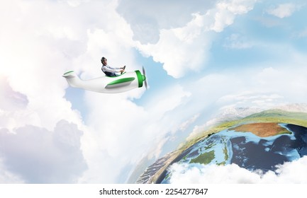 Aviator in leather helmet driving small propeller plane in cloudy blue sky. Extreme aviation hobby and free time activity. Funny man flying in small airplane. Earth globe horizon with sea line - Shutterstock ID 2254277847