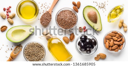 Avocado, almonds, hemp seeds, linseeds, olives and oils over white background, top view. Alternative oils concept