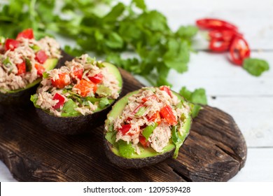 Avocado appetizers stuffed with canned tuna, bell pepper, herbs on wooden cutting board