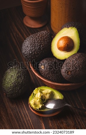 Avocado in a clay plate against a dark and moody wooden backdrop. This trendy composition creates a visually appealing contrast. Scraped avocado with half a spoon. Healthy Eating, Dark Moody style.