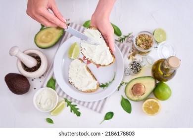 Avocado and cream cheese toasts preparation - Woman smearing cheese on a grilled or toasted bread - Shutterstock ID 2186178803