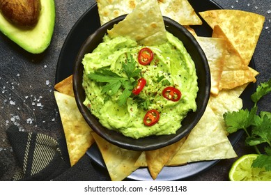 Avocado dip guacamole with tortilla chips in a black bowl on a dark slate or metal background.Top view. - Powered by Shutterstock