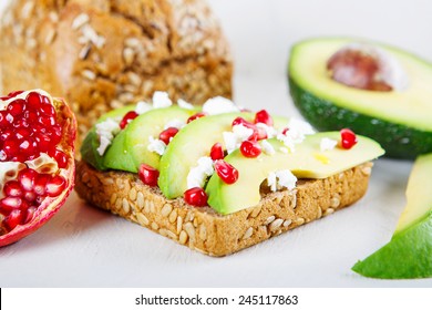 Avocado With Feta, Pomegranate And Olive Oil On Sunflower Seeds Bread Sandwich. Healthy Organic And Vegan Breakfast, On White Wooden Background