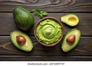 Avocado with guacamole sauce on a dark wood background. Half and whole avocados are close. View from above. Copy space