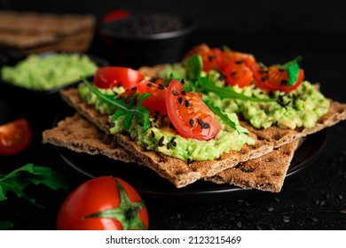 Avocado sandwich with avocado cream and rye crisp bread for snack. Fiber, fitness and diet food. Rye bread with guacamole, arugula and cherry tomatoes on dark background. High quality photo