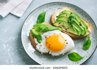 Avocado Sandwich with Fried Egg - sliced avocado and  egg on toasted bread with arugula for healthy breakfast or snack.