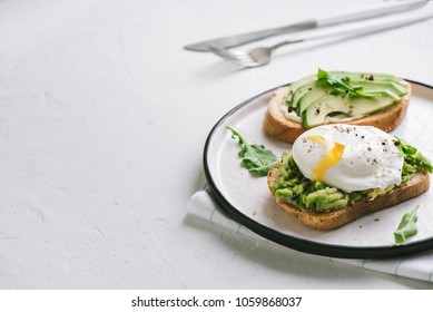 Avocado Sandwich with Poached Egg - sliced avocado and egg on toasted bread for healthy breakfast or snack, copy space.