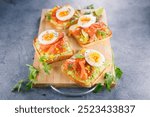 Avocado, smoked salmon, and egg on toast served on a wooden board. Perfect for healthy breakfasts and gourmet meals