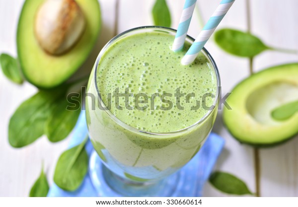 Avocado and spinach green smoothie on a light\
wooden table.