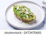 Avocado toast with feta and pistachio on a plate, white marble background.