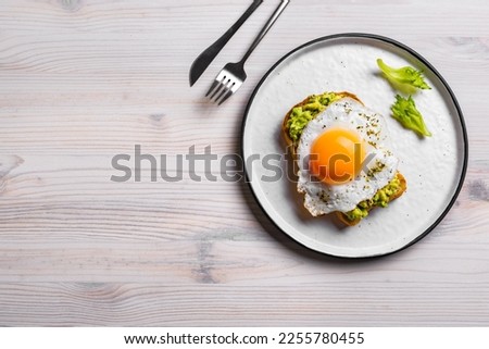 Avocado toast with fried egg on wooden table, top view, copy space. Toasted bread with avocado and egg for healthy breakfast.