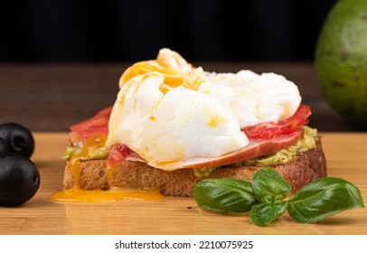 Avocado Toast With Ham And Poached Egg Yolk On A Cutting Board.. Copy Space.