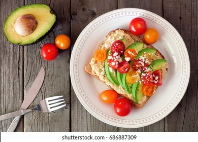 Avocado toast with hummus and tomatoes on plate, above scene on old wood background - Powered by Shutterstock