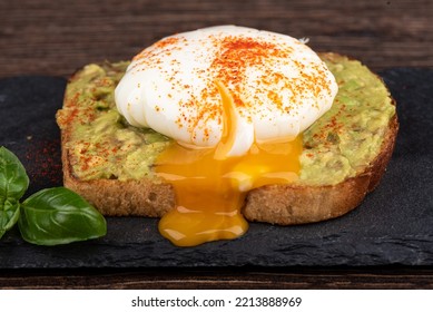 Avocado Toast With Leaking Poached Egg Yolk On A Stone Board For Serving. Close Up.