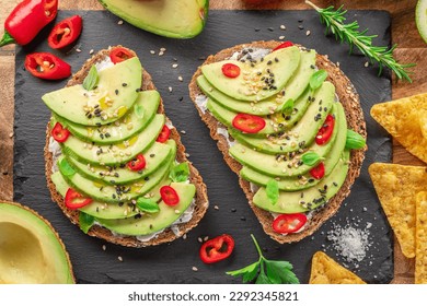 Avocado toasts - bread with avocado slices, pieces of red pepper and sesame on black stone board. - Powered by Shutterstock