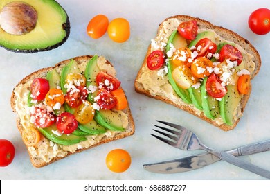 Avocado toasts with hummus and tomatoes, overhead view on white marble background - Powered by Shutterstock