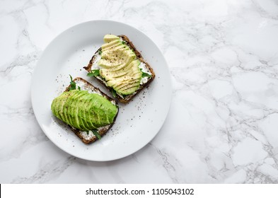 Avocado toasts on rye bread with sliced avocado, arugula, creme cheese with salt and pepper for healthy breakfast on light marble background. Vegetarian food. Clean eating. Top view. Copy space. - Powered by Shutterstock