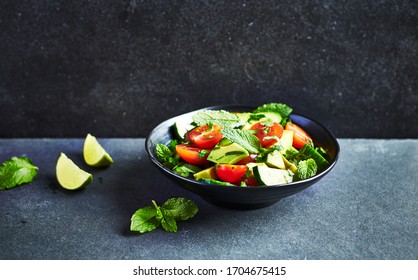 Avocado, tomato and cucumber salad with fresh herbs on dark stone background. Healthy summertime salad. Copy space - Shutterstock ID 1704675415