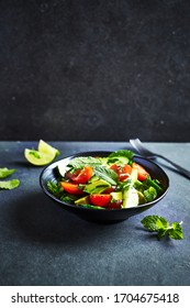 Avocado, tomato and cucumber salad with fresh herbs on dark stone background. Healthy summertime salad. Copy space - Shutterstock ID 1704675418