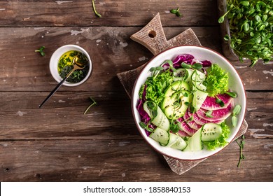 avocado and watermelon radish salad with mix of lettuce leaves and microgreen, cabbage, cucumber on a white dish, Healthy food. Vegetarian buddha bowl. Top view. Flat lay.