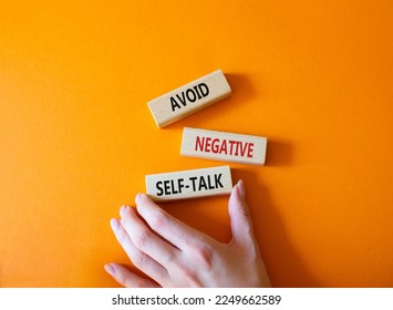 Avoid negative self-talk symbol. Concept words Avoid negative self-talk on wooden blocks. Businessman hand. Beautiful orange background. Business and Avoid negative self-talk concept. Copy space.