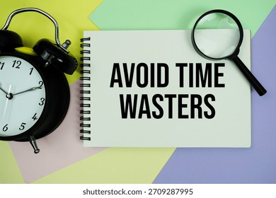 Avoid Time Wasters text written on notepad with alarm clock and magnifying glass on pastel background