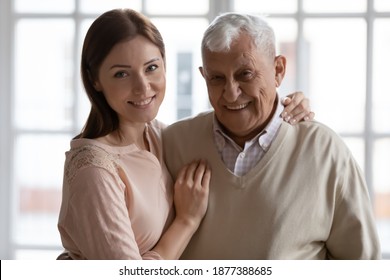 Awaited Guest. Happy Laughing Older Father And Young Woman Grown Daughter Stand Hug Look At Camera. Retired Grandfather Posing For Portrait Embracing Adult Granddaughter Proud With Beloved Offspring