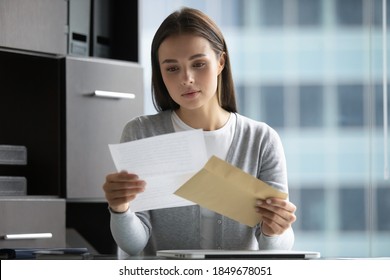 Awaited news. Attentive interested young female office worker manager businesswoman holding in hands paper letter and envelop received by mail reading important information thinking on offer benefit