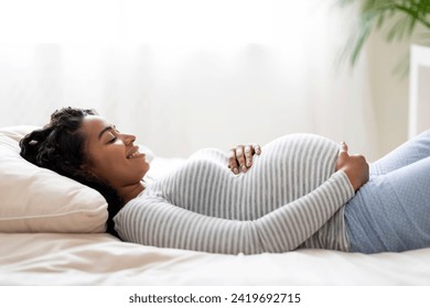 Awaiting Baby. Happy Young Black Pregnant Woman Touching Belly While Lying On Bed In Bedroom, Smiling Beautiful African American Expectant Mother Relaxing At Home, Enjoying Pregnancy Time, Side View - Powered by Shutterstock