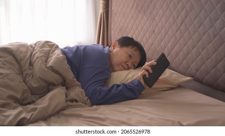 Awake Elderly Old Asian Woman, People Waking Up, Using A Smartphone On Social Media Internet And Sleeping On Bed In Bedroom At Home. Lifestyle In Technology Device Concept In Morning.