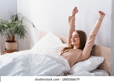 Awake And Joyful Woman In Satin Pajamas Stretching In Bed