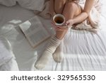 Awakened Woman Sitting on the edge of the Bed looking out the Window, bare Feet on the Floor. Side view, cropped Photo of Beautiful Female Legs. Spring rays of the sun penetrate through wooden blinds