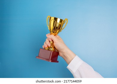 Award Cup In Hand, Gold Prize, Winner Trophy On Blue Background