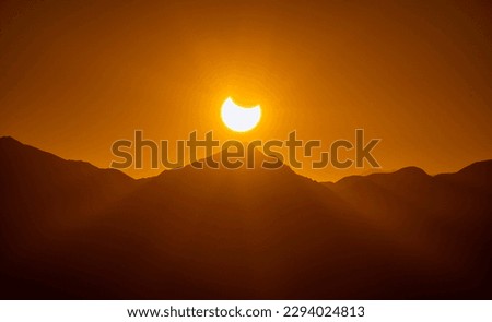 An awe-inspiring photo of a solar eclipse viewed from a mountainous landscape. The dark silhouette of the moon obscures the sun, creating a striking halo effect around the edges of the eclipse.