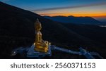 An awe-inspiring view of a big golden Buddha statue atop a hill overlooking a serene valley, captured during the vibrant colors of sunset. aerial view of The biggest golden Buddha at Lopburi Thailand