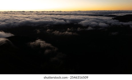 An awe-inspiring view of the sunset casting warm hues above a dense cloud layer over mountains, creating a serene and dramatic atmosphere. - Powered by Shutterstock