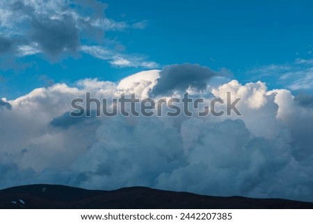 Awesome cloudy view to huge dramatic lush clouds in blue sky. Beautiful cloudscape with mountain silhouettes. Scenic skyscape with cirrus clouds. Atmospheric landscape with fluffy unusual cloudy skies