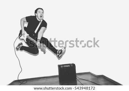 Awesome crazy fashion young rock guitar player jumps with passion in studio. Black and white toned. White background.