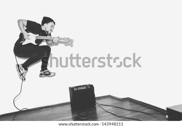 Awesome\
crazy fashion young rock guitar player jumps with passion in\
studio. Black and white toned. White\
background.
