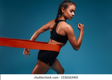 Awesome Girl Stretching Band During Her Pilates Training. Close Up Back View Photo. Isolated Blue Background, Studio Shot.