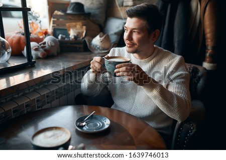 awesome man sitting in caffe and drinking hot tea in front of window, close up side view photo, good morning, good day with tasty coffee