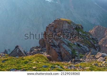 Awesome mountain landscape with cliff above abyss. Beautiful scenery with green grass near sharp rock near precipice edge. Scenic sunny view to green cliff with sharp stones at very high altitude.