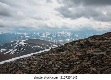 Awesome view from stone hill with sharp stones to snow mountains under cloudy sky. Alpine landscape at very high altitude with cloudiness. Atmospheric scenery with snowy mountain range in overcast.