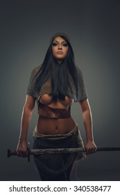 Awesome woman with long black hair in ancient knight clothes holding sword. Isolated on grey background.
