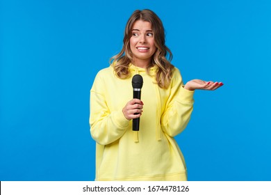 Awkward Cute Blond Girl Dont Know Lyrics As Singing Karaoke, Looking At Friend Nervous Smile, Embarrassed Sing In Fron Of People, Hold Microphone, Standing Blue Background