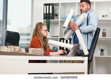 An Awkward Office Worker Scattering Drawings On The Table Of His Serious Disgruntled Female Manager.