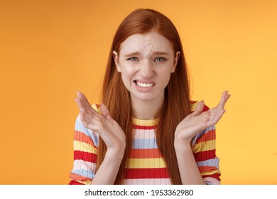 Awkward unhappy worried young redhead girl cringe feel sorry apologizing smirking smiling nervously frowning squinting spread hands sideways shrugging confused, standing orange background