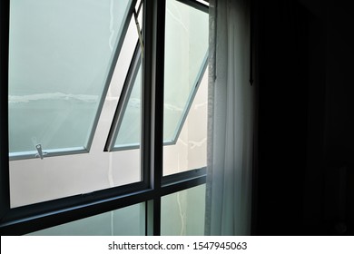 Awning Window frame that has white curtain on the side in the low light room.