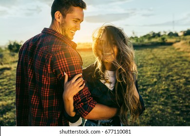 Awsome happy couple have fun in a field sunset background. Handsome Caucasian guy wearing plaid shirt gentle hugs a smiling girl with blond hair in plaid shirt. Lifestyle and travel concept. - Powered by Shutterstock